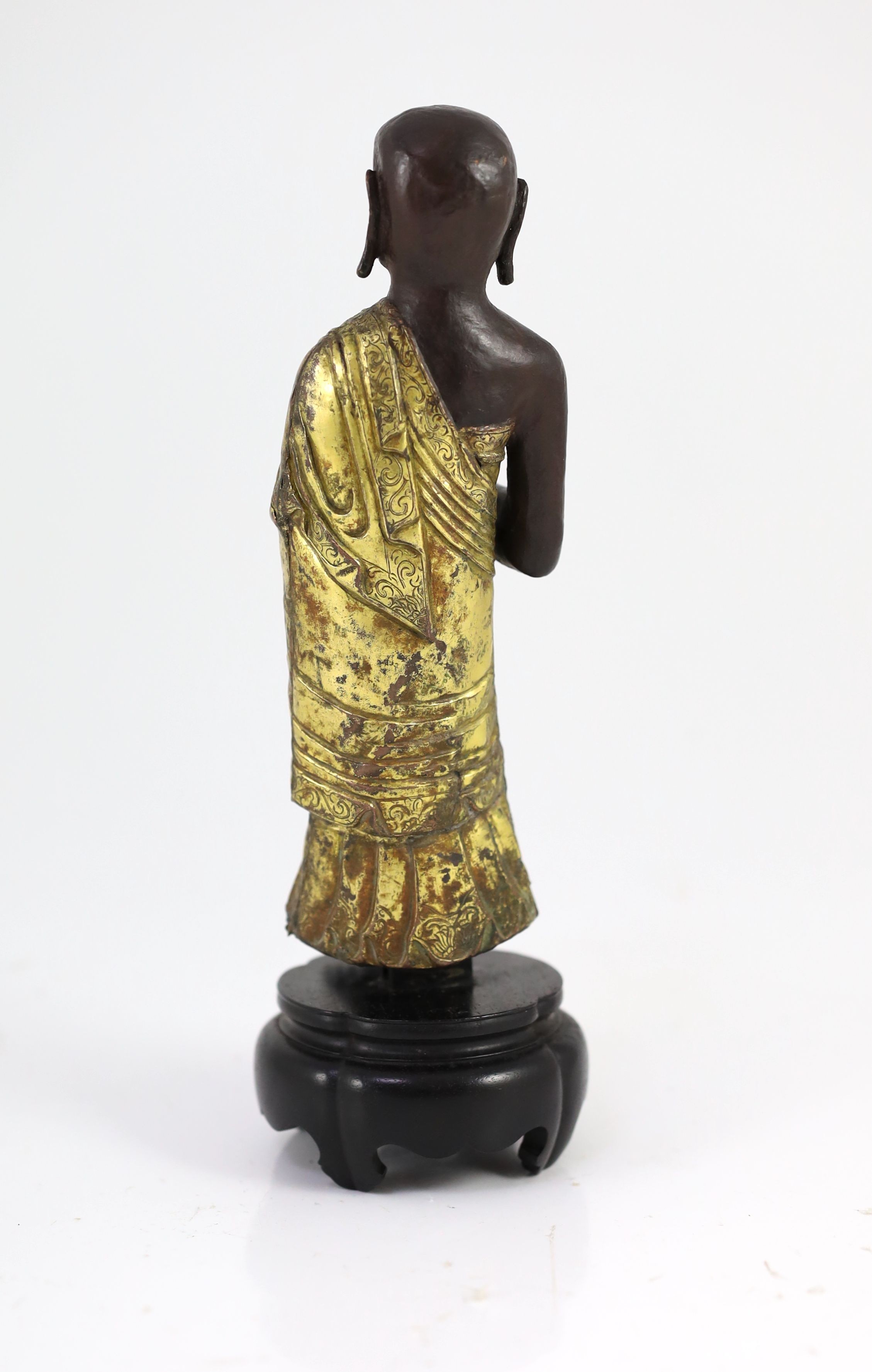 A Tibetan repousse work gilt and lacquered copper figure of a luohan, 18th century, 20.5 cm high, wood stand